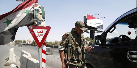 Un soldat syrien tient un poste de contrôle devant un portrait de Bachar al-Assad sur l’autoroute de Mezzeh à Damas en 2014.