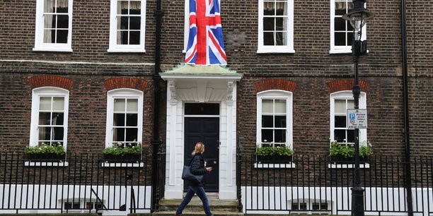 Woman walks past a union jack flag hanging on a house in westminster in london[reuters.com]