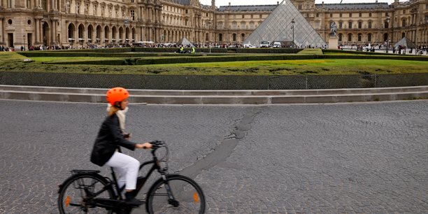 Une femme circule en velo pres de la pyramide du musee du louvre a paris[reuters.com]