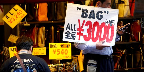 Un employe de magasin tient une pancarte pour attirer les clients a tokyo[reuters.com]