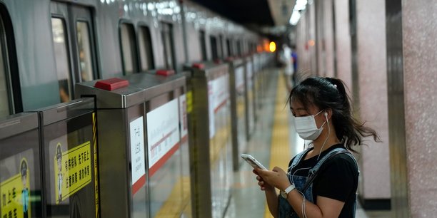 Une femme portant un masque regarde son smartphone en attendant le metro a pekin[reuters.com]