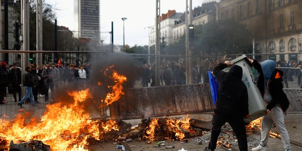 Photo des gens qui portent une poubelle a cote d'un incendie lors d'affrontements pendant une manifestation pour protester contre l'article 49.3 de la constitution[reuters.com]