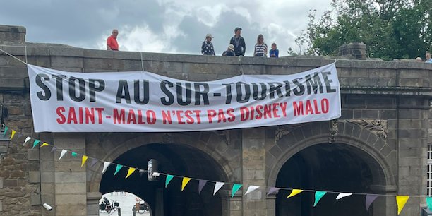 Dimanche 16 juillet au matin, une large banderole a été déroulée en haut des remparts de la vieille ville de Saint-Malo (Ille-et-Vilaine) pour dénoncer le surtourisme. (@SoLeNoenLess)