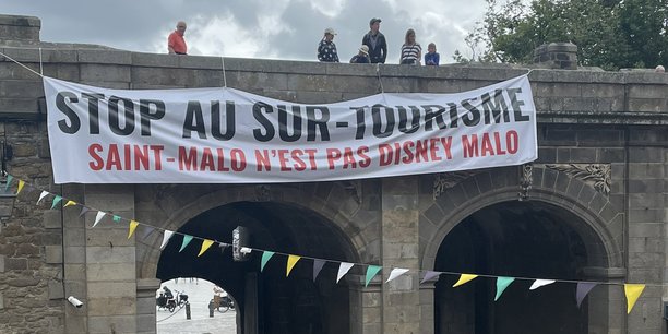 Le 16 juillet dernier, une large banderole a été déroulée en haut des remparts de la vieille ville de Saint-Malo (Ille-et-Vilaine) pour dénoncer le surtourisme. (@SoLeNoenLess) (Crédits : Twitter)