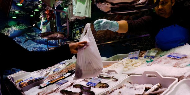 Un poissonnier tend un sac a un client dans un supermarche a madrid[reuters.com]