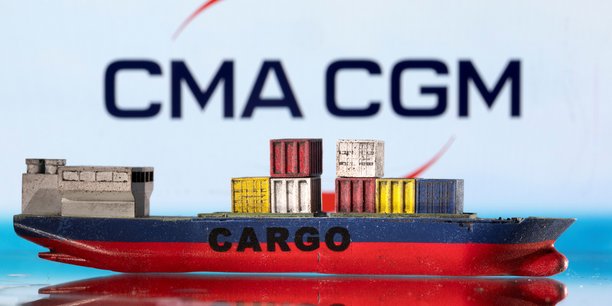 Un modele de bateau cargo est photographie devant le logo de cma cgm.[reuters.com]