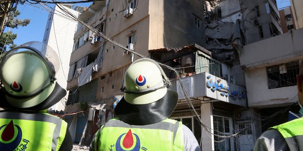 Des membres de la defense civile se tiennent pres d'un batiment endommage au lendemain d'une frappe israelienne a beyrouth[reuters.com]