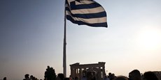 Le drapeau grec flotte au vent au-dessus de touristes visitant le site archéologique de l'Acropole à Athènes, en Grèce