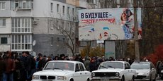 Des personnes attendent la distribution d'aide humanitaire, avec un panneau publicitaire pro-russe en arrière-plan, à Kherson