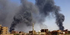 Un homme marche tandis que de la fumée s'élève au-dessus des bâtiments après un bombardement aérien à Khartoum