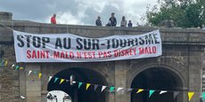 Dimanche 16 juillet au matin, une large banderole a été déroulée en haut des remparts de la vieille ville de Saint-Malo (Ille-et-Vilaine) pour dénoncer le surtourisme. (@SoLeNoenLess)