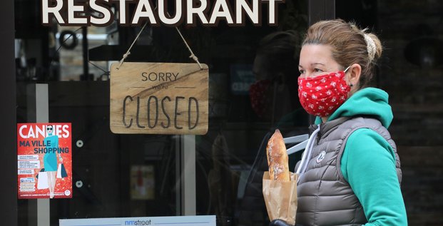 Fermeture commerce restaurant. Une femme portant un masque et une baguette passe devant un restaurant fermé à cause de l'épidémie de coronavirus, le 16 avril 2020 à Cannes