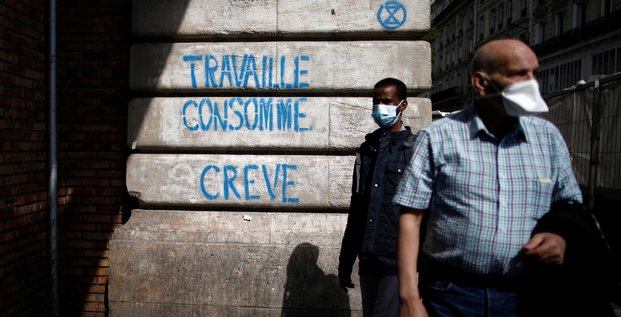 Coronavirus : deux personnes portant un masque passent devant un slogan disant : Travaille, consomme, crève (à Paris)