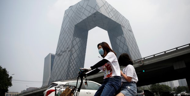 Chine : une femme portant un masque roule en vélo électrique devant le siège de la Télévision centrale de Chine à Pékin le 16 juillet 2020