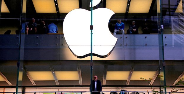 Un client se tient sous un logo apple illumine alors qu'il regarde par la fenetre du magasin apple situe dans le centre de sydney