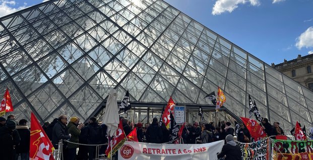 Des manifestants portant des drapeaux cgt et sud culture solidaires se tiennent devant la pyramide du louvre