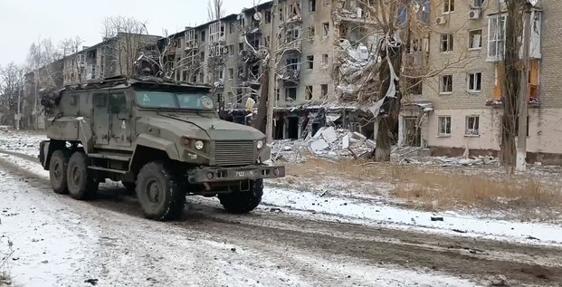 Un vehicule militaire russe passe devant des batiments residentiels endommages dans la ville d'avdiivka