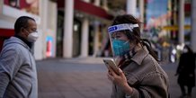 Une femme portant un masque de protection et un ecran facial marche a shanghai, en chine