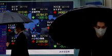 Des hommes passent devant un tableau electrique affichant les indices nikkei et d'autres pays devant une maison de courtage a tokyo