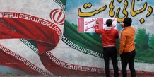 Des hommes iraniens placent des affiches de campagne sur un mur lors du dernier jour de la campagne electorale a teheran